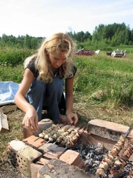 Young longhaired blonde woman roasting meat on fire Stock Photos