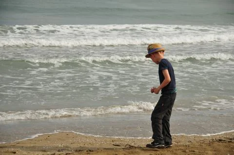 Young looks for shells at the sandy beach directly at the water in the vacati Stock Photos
