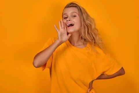 Young loud Caucasian woman puts hand to mouth and shouts stands in studio Stock Photos