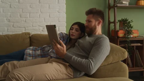 Young love couple lying together on couch, watching tablet Stock Footage 266802414