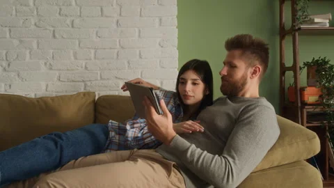 Young love couple lying together on couch, watching tablet Stock Footage 266802471