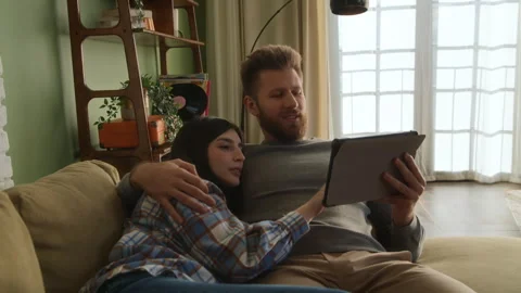Young love couple lying together on couch, watching tablet Stock Footage 266802995