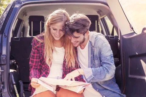 Young lovers looking map sitting in the trunk of car Stock Photos