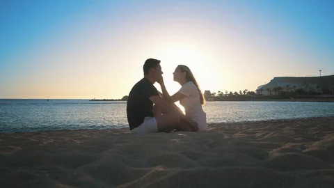 A young loving couple is sitting on a sandy beach near the sea at sunset. Girl Stock Footage 104198266