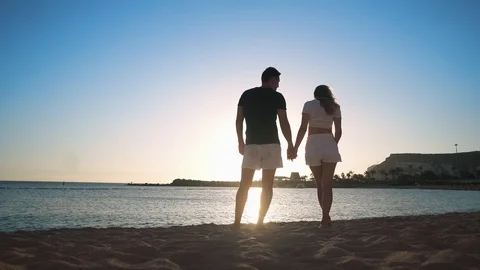 A young loving couple is standing on a sandy beach near the sea at sunset Stock Footage 104202063