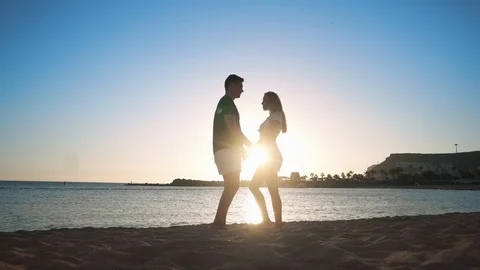 A young loving couple is standing on a sandy beach by the sea at sunset opposite Stock Footage 104202461