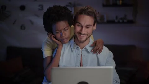Young loving multiracial couple using laptop and surfing internet to book Stock Footage 264126760