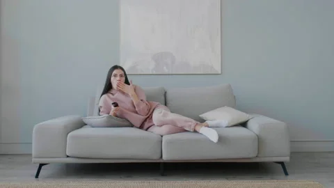 A young lying on the sofa, yawning, smiling and changing TV channels. Stock Footage 148528937