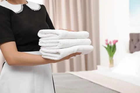 Young maid holding stack of fresh towels in hotel room, closeup 스톡 사진