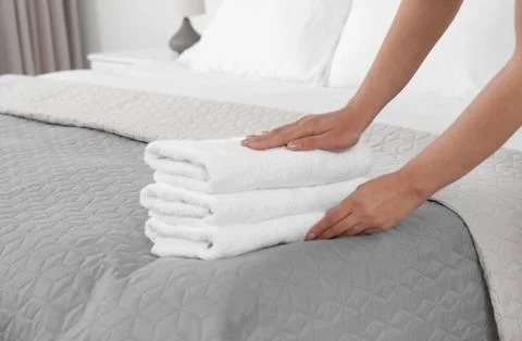 Young maid putting stack of fresh towels on bed in hotel room, closeup Foto stock