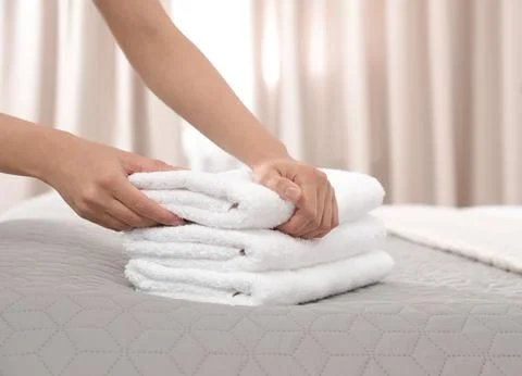 Young maid putting stack of fresh towels on bed in hotel room, closeup 스톡 사진