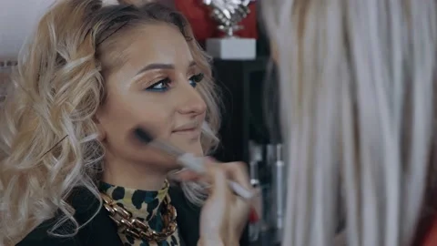 The young make-up artist in the mini studio at home applies blush on the blonde Stock Footage 157556783