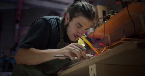 Young male artisan making marks on wood for musical guitar instrument at Stock Footage 137241816