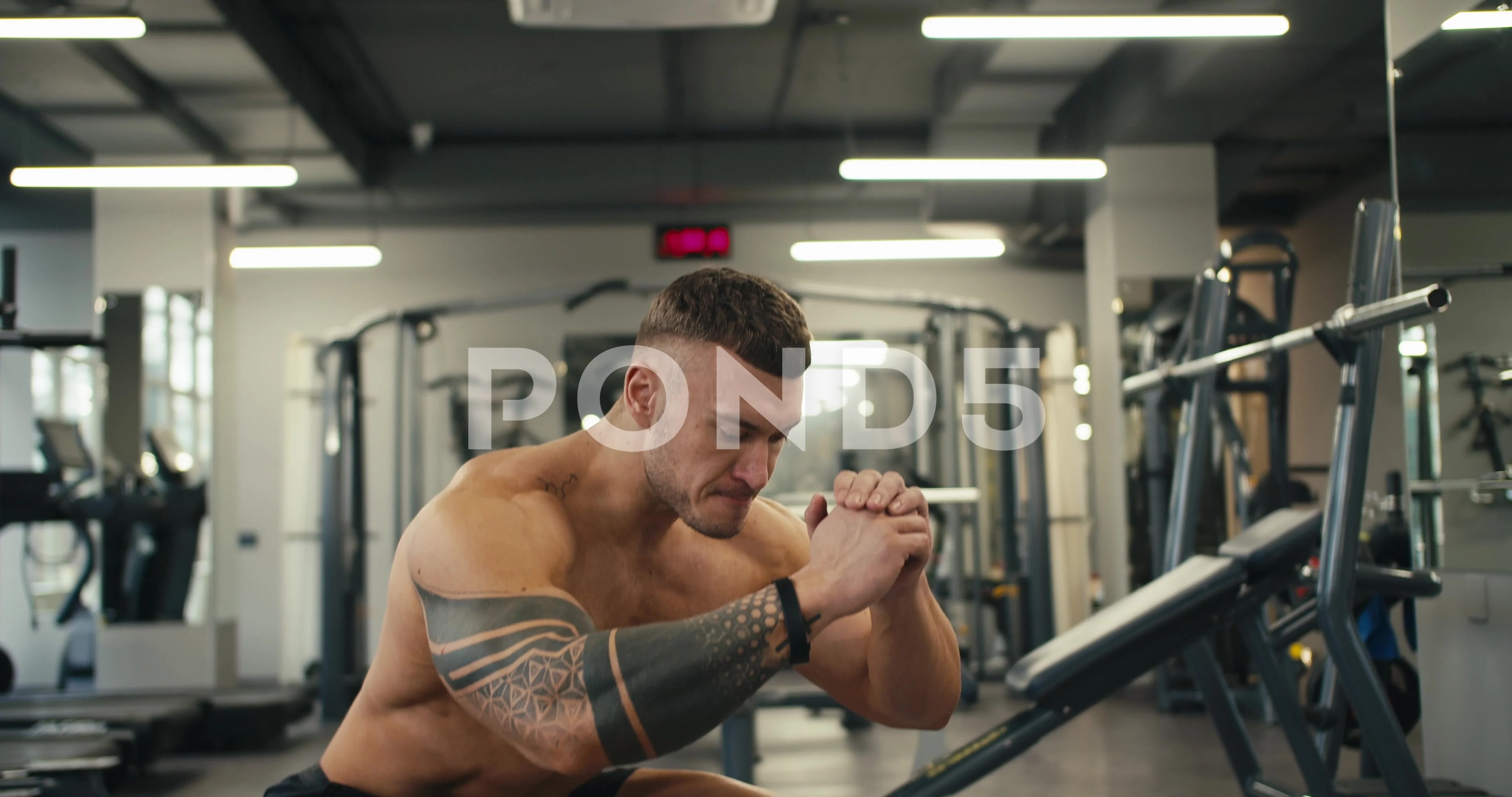 A young male athlete with a naked torso and a tattoo performs squats while  in