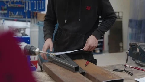 Young male blacksmith apprentice measures a piece of metal with a Stock Footage 246292382