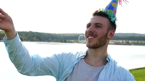 Young male blowing soap-bubbles on the lake background. Stock Footage