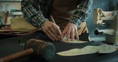 Young male bootmaker cutting out leather pieces on table at the workshop. Stock Footage 246307273