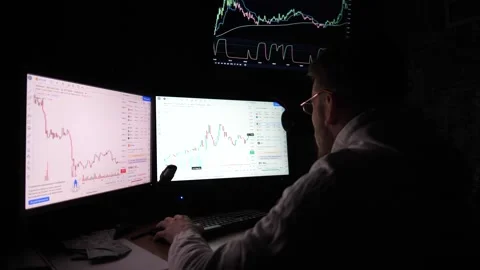 Young male broker analyzing graphs on multiple computer screens. Financial Stock Footage 309299360
