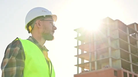 Young male builder engineer architect foreman with beard straightens his white Stockbeeldmateriaal 201364759