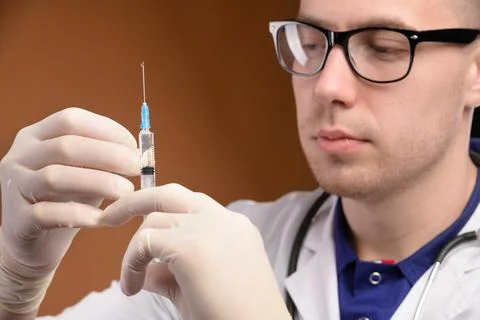 Young male Caucasian doctor in a glass holds a syringe with an injection with Stock Photos