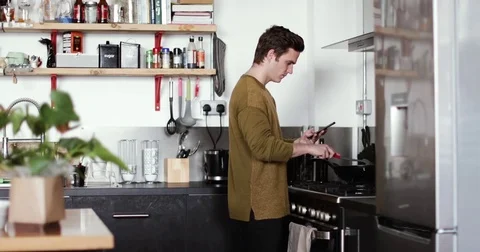 Young male cooking in kitchen using smartphone Stock Footage 85203407