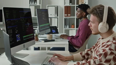 Young Male Developer in Headphones Coding on Computer in Open Plan Office Video stock 330128052