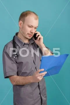 Young male doctor holding a folder with papers and talking on the phone on blue Stock Photos