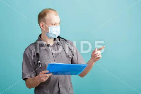 Young male doctor holding a folder with papers on blue background Stock Photos