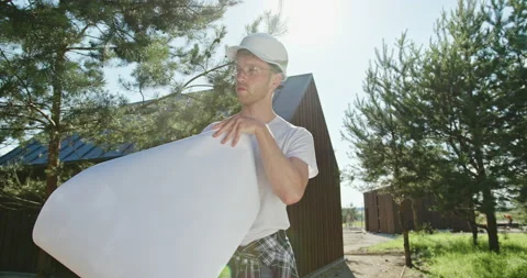 Young male engineer in hardhat unrolling and examining draft while working in Stock Footage 141128470
