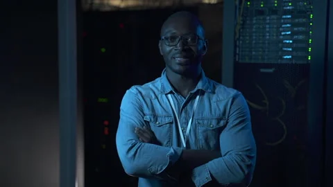 Young male engineer posing and smiling while standing in dark room of data Stock Footage 159794855