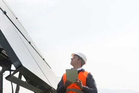 Young male engineer using digital tablet looking up at solar panels Stock Photos
