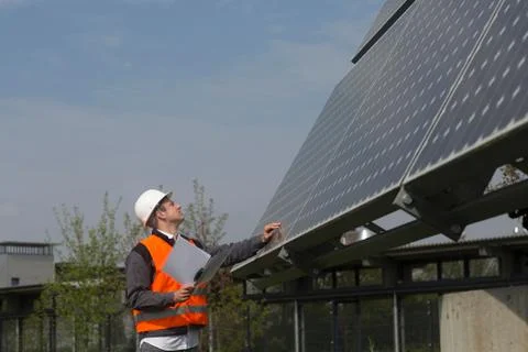 Young male engineer using digital tablet looking up at solar panels Stock Photos