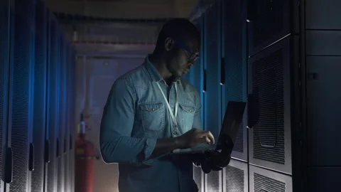 Young male engineer working with laptop hardware while standing in render farm Stock Footage 160805532