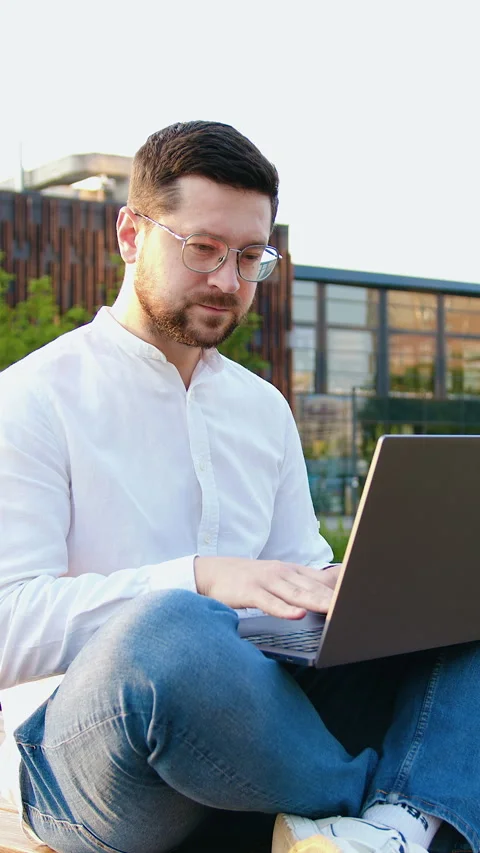 Young male freelancer working computer at modern glass building background outdo Stock Footage 327546983