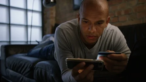 Young male on his couch using his phone and credit card for online shopping Video stock 96342807
