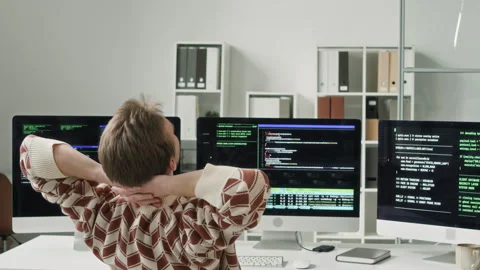 Young Male IT Engineer Stretching Arms while Reviewing Code on Screens in Office Stock Footage 330132333