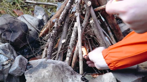 Young male making a small forest campfire using sticks and warming up his hands Stock Footage 195306901