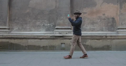 Young male person dancing while using smartphone and walking at old city street Stock Footage