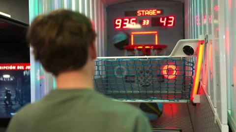 Young male player engaging in competitive basketball arcade game with vibrant Vídeos de archivo 316495454