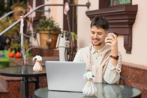 Young male programmer with coffee and laptop working at table in street cafe Stock Photos