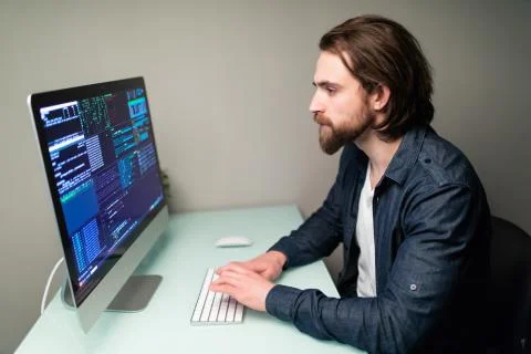Young Male programmer working on desktop computer at white desk in office. Stock Photos
