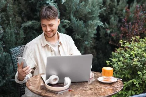 Young male programmer working with laptop and mobile phone at table in street Stock-Fotos
