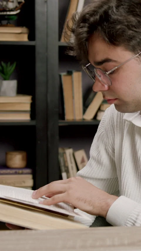 Young male reader in white sweater examines pages of an open book while seated Stock-Footage 332474589