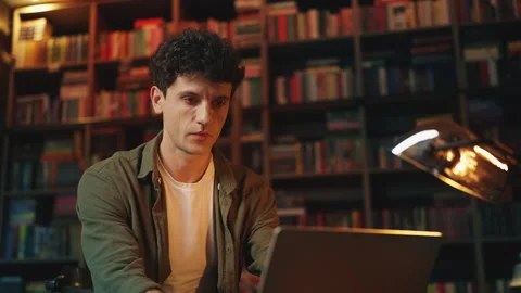 Young male scientist researching online material on laptop in a library Stock Footage 340266260