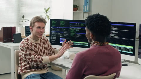 Young Male Senior Developer Mentoring Junior Colleague at Computer Desk Stock Footage 330131620