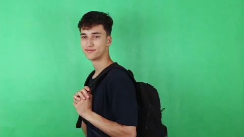 Young male student with black backpack stands in profile against green backdrop Stock Footage 329478330
