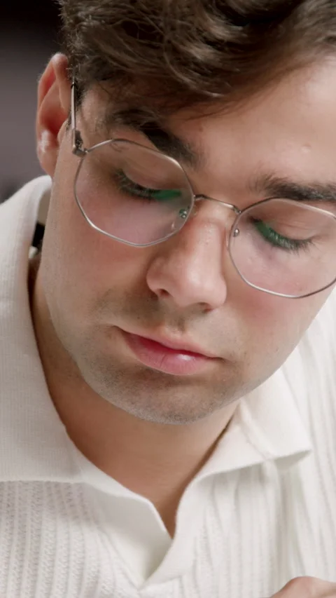 Young male student with glasses writes notes with pencil on paper, surrounded by Stock-Footage 332473853