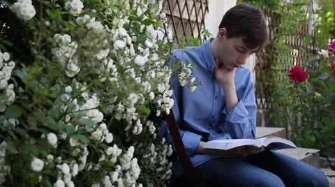 Young male student learning from a book in a rose garden, study, exams Stock Footage 39654870