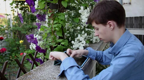 Young male student using tablet computer on home terrace, flowers Stock Footage 39655599