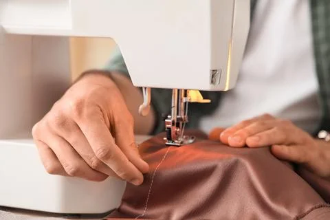 Young male tailor using sewing machine in atelier, closeup Stock Photos